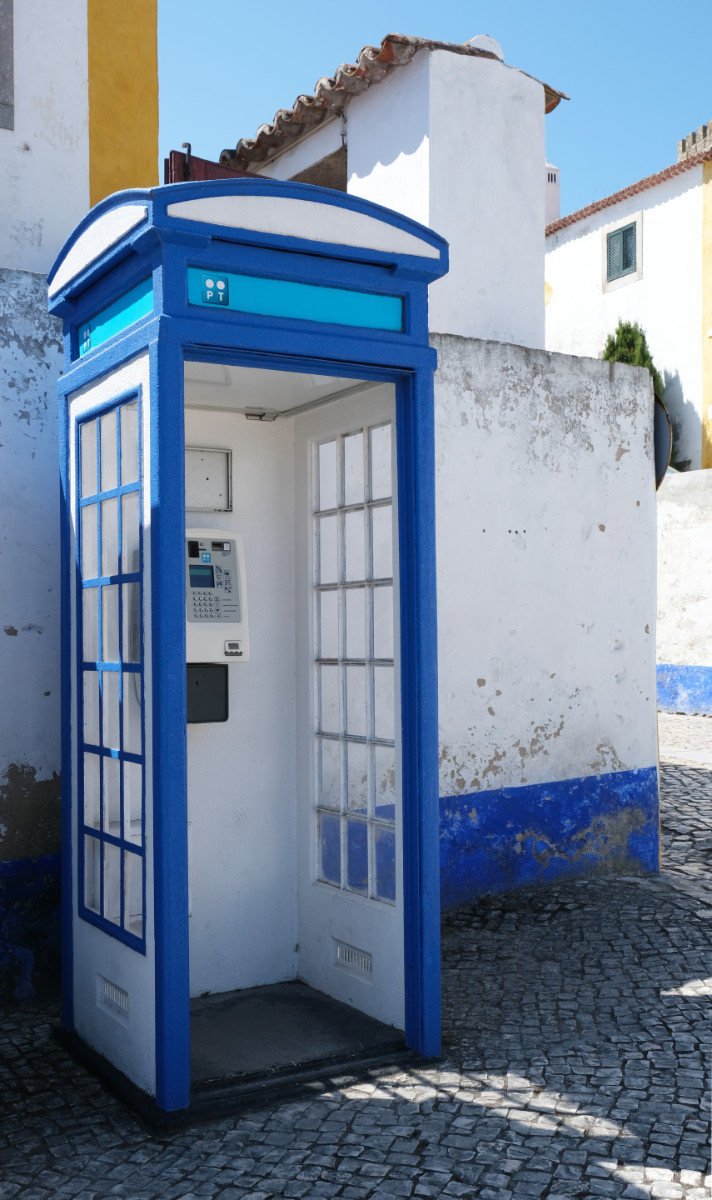 A blue Portuguese phone box against a white and yellow wall