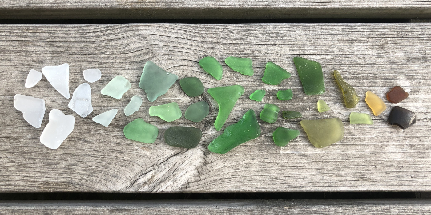Sea glass from white to green to yellow to dark brown to light, laid out on weathered wood planks
