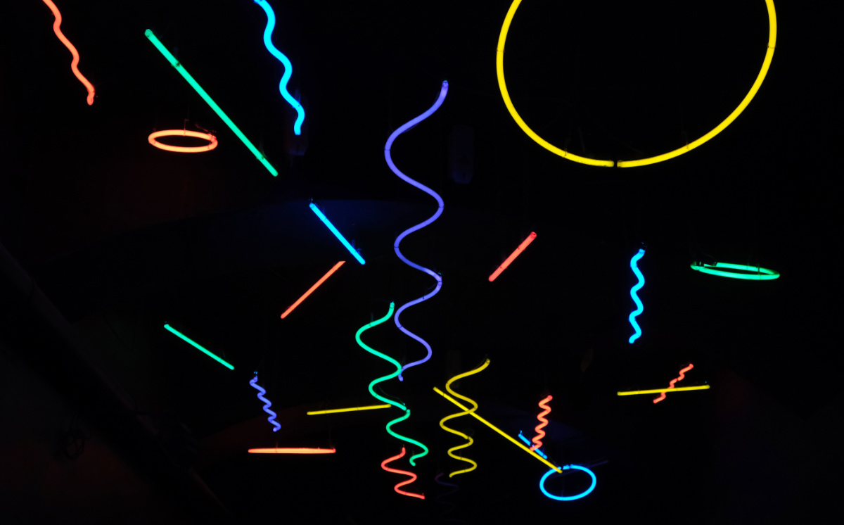 Multi-coloured neon lights, wavy, straight, and circular, stretching down a black expanse in LX Factory, Lisbon.